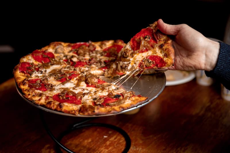A fire-roasted LouEddie's pizza, a slice being lifted from the pan